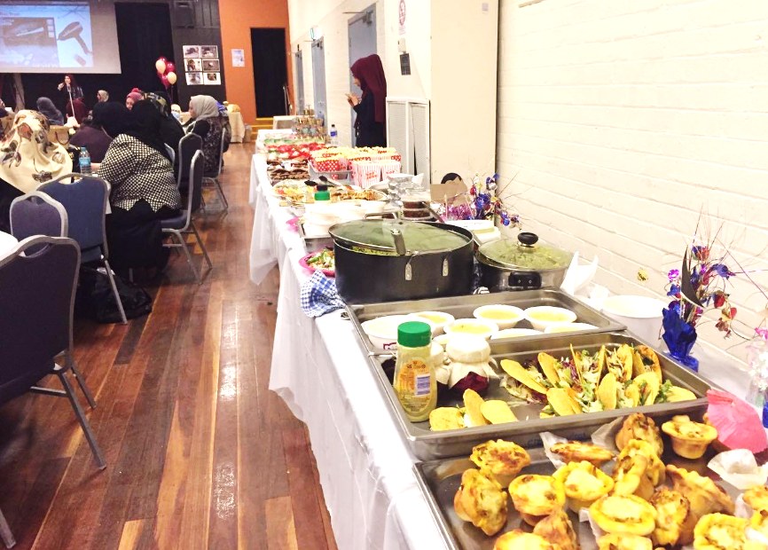 Women gathered at a community event hosted by Bint Al-Huda, with a buffet of home-cooked food